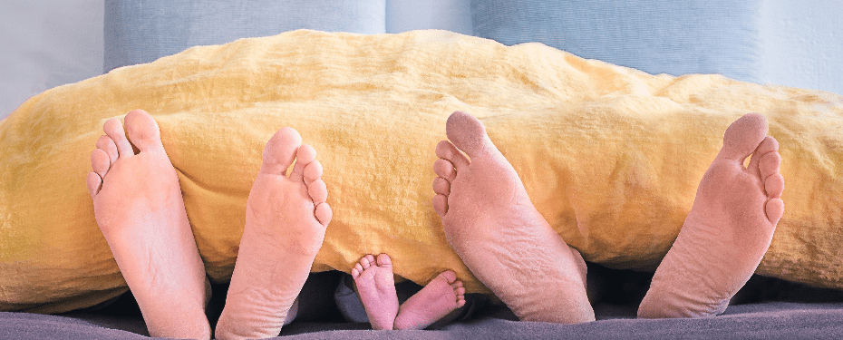 A close-up of adult and baby feet peeking out from under a yellow blanket, symbolizing family bonding and togetherness in a cozy home setting.