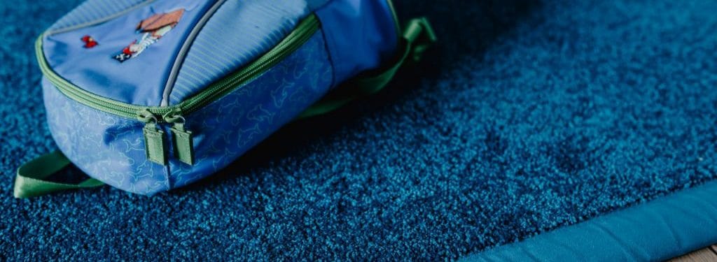 Close-up of a blue backpack with green accents resting on a textured blue surface, highlighting its vibrant color and design.