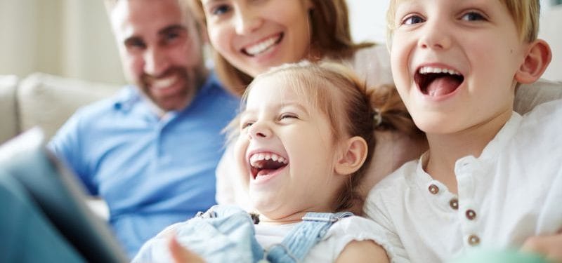 A happy young girl laughing joyfully while sitting with her smiling family members, showcasing a moment of togetherness and joy.