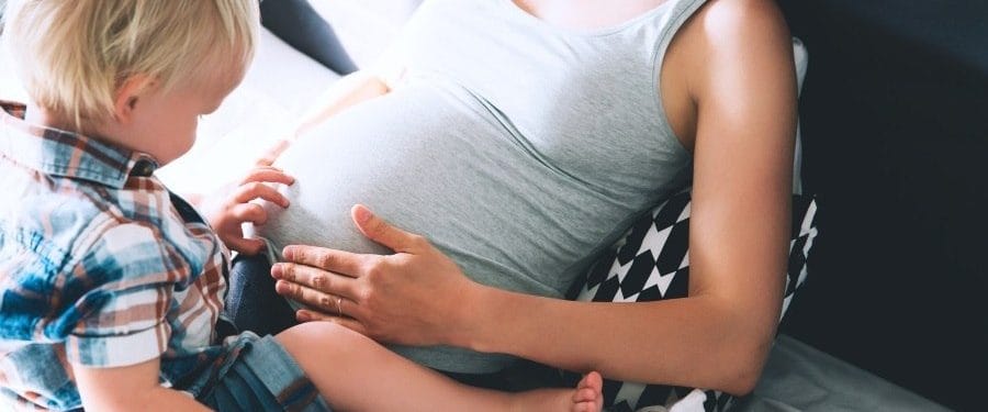 Pregnant woman gently cradling her baby bump while sitting on a couch, showcasing maternal love and anticipation.