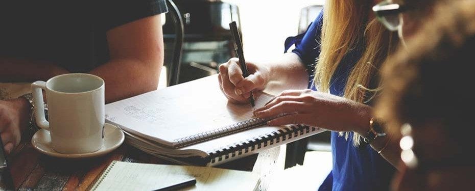 A close-up of a person's hand writing in a sketchbook, showcasing creativity and artistic expression in a casual setting.