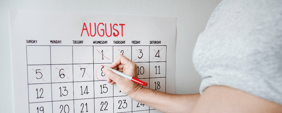 Hand marking a date on an August calendar with a red marker, showcasing organization and planning.
