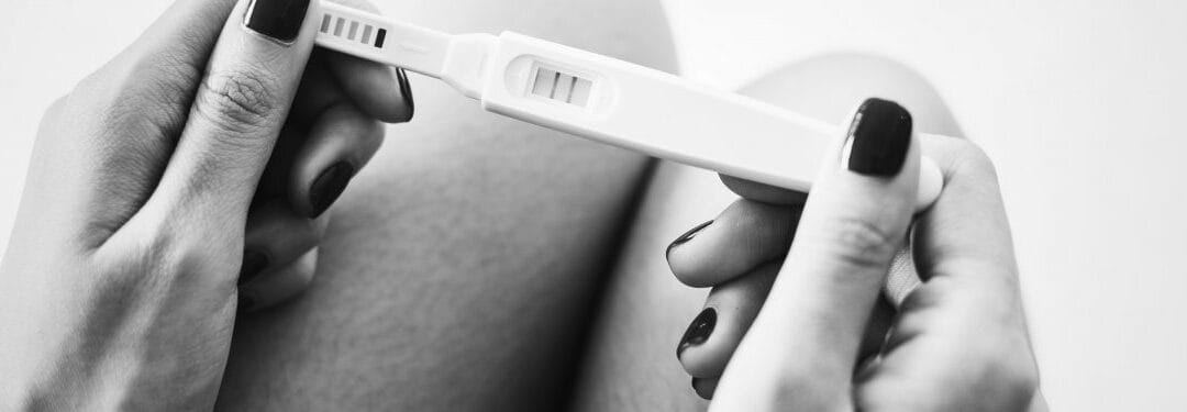 Close-up of a woman holding a pregnancy test with a positive result, showcasing the test display and her hand with dark nail polish.
