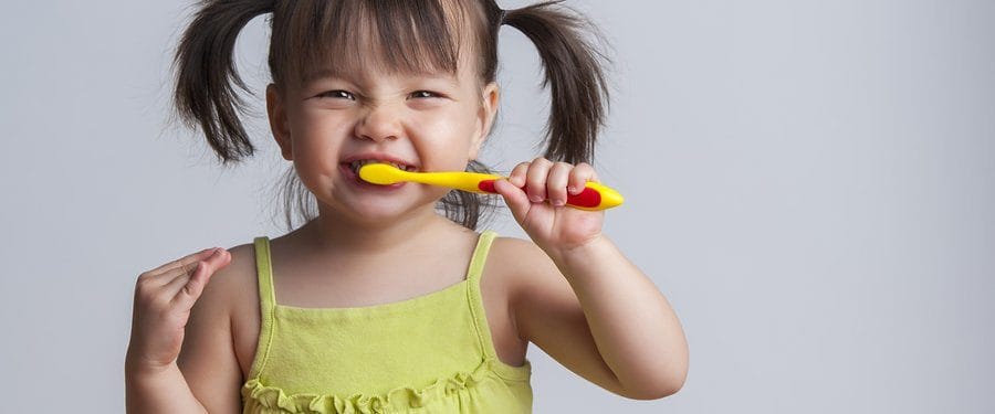 Smiling young girl with pigtails holding a yellow toothbrush, promoting good dental hygiene for children.