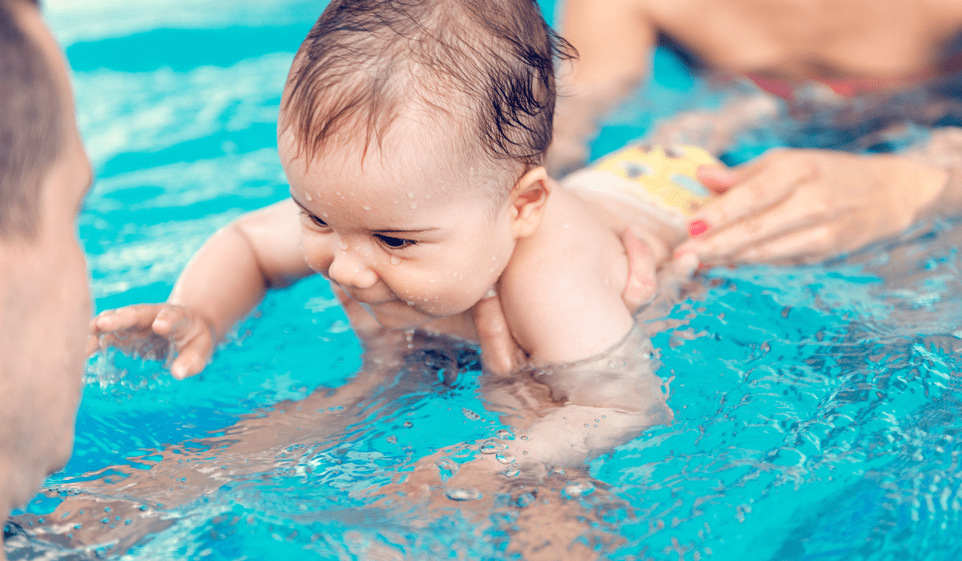 Baby swimming in a pool, exploring the water with playful curiosity while being supported by an adult.