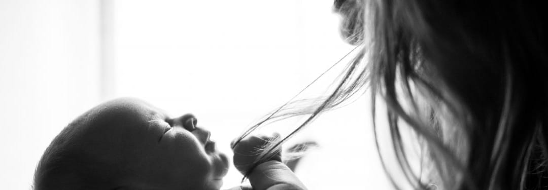 Black and white image of a baby reaching for a woman's hair, capturing a tender moment of connection and curiosity.