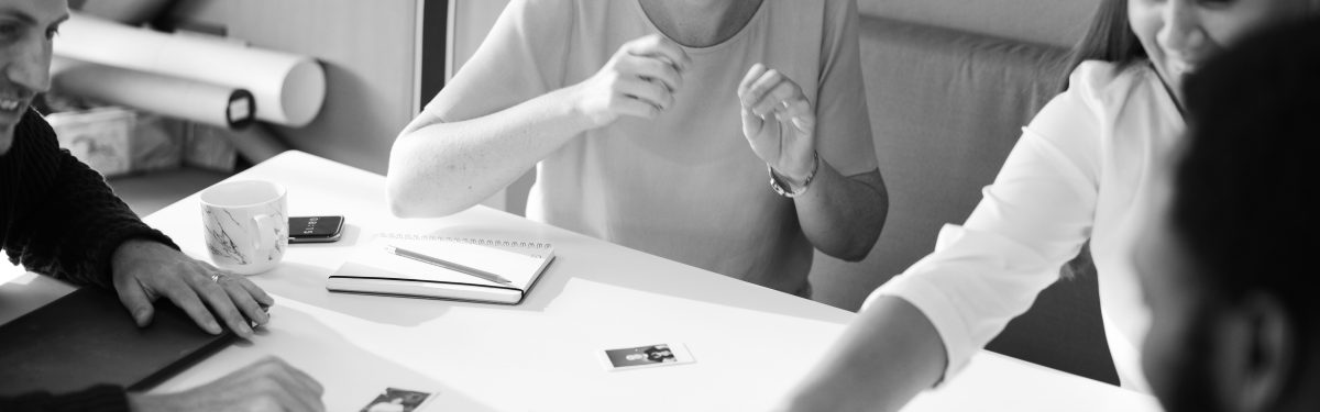 pente-tips-gia-tin-proti-gnorimia-me-ti-daskala-to-daskalo Person gesturing during a discussion at a table, with a notebook and a small photograph visible, in a black and white setting.