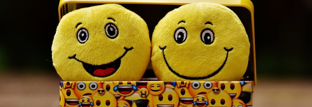synaisthimatiki-noimosyni-ti-eidoys-exypnada-einai-ayti-einai-simantiki-gia-to-paidi-moy Two cheerful yellow emoji plush toys with smiling faces, displayed against a colorful background featuring various emoji patterns.